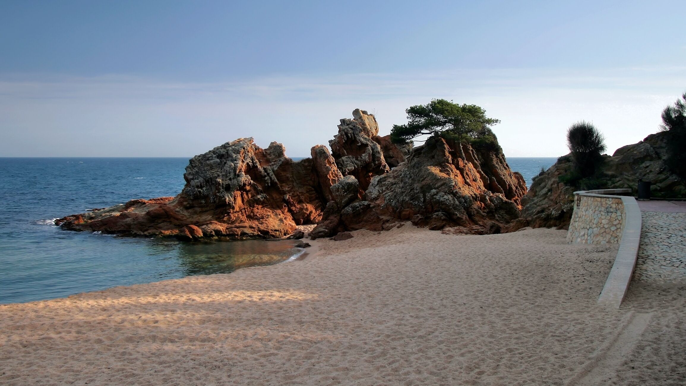Eine felsige Küstenlinie mit einem Sandstrand und einer Steinmauer.