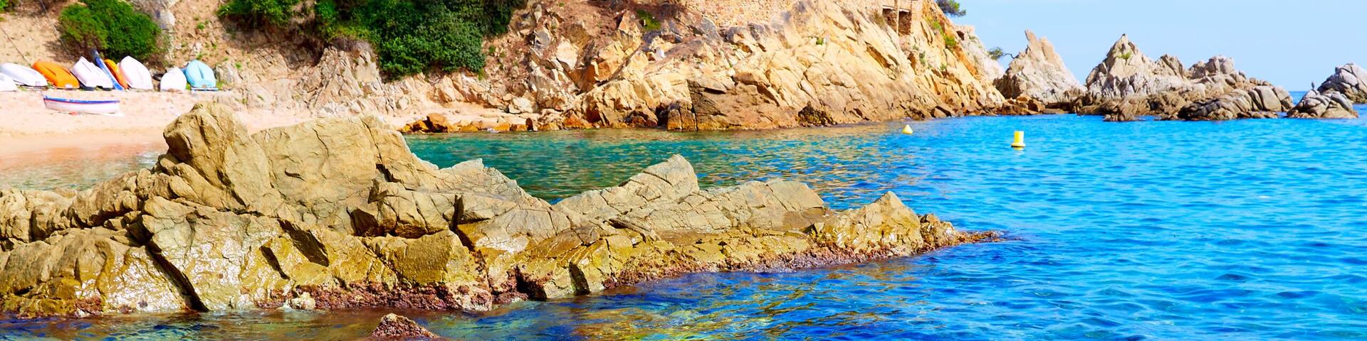 A coastal landscape with clear blue waters, rocky shorelines, and a castle perched on a cliff.