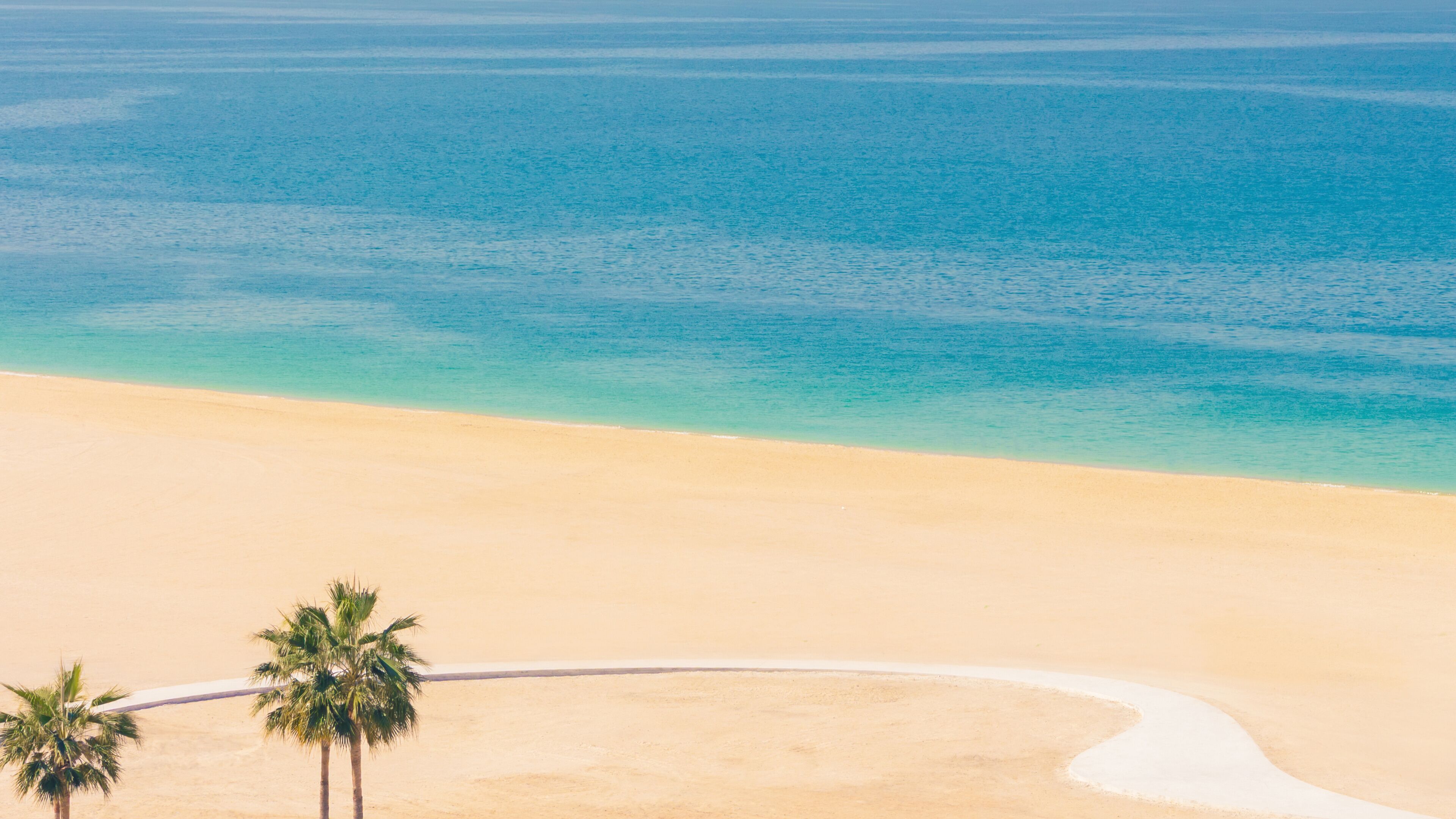 Wide 16:9 panoramic view of Ajman beach with turquoise sea, golden sand, UAE. Aerial resort coastline banner background, palm trees, copy space.