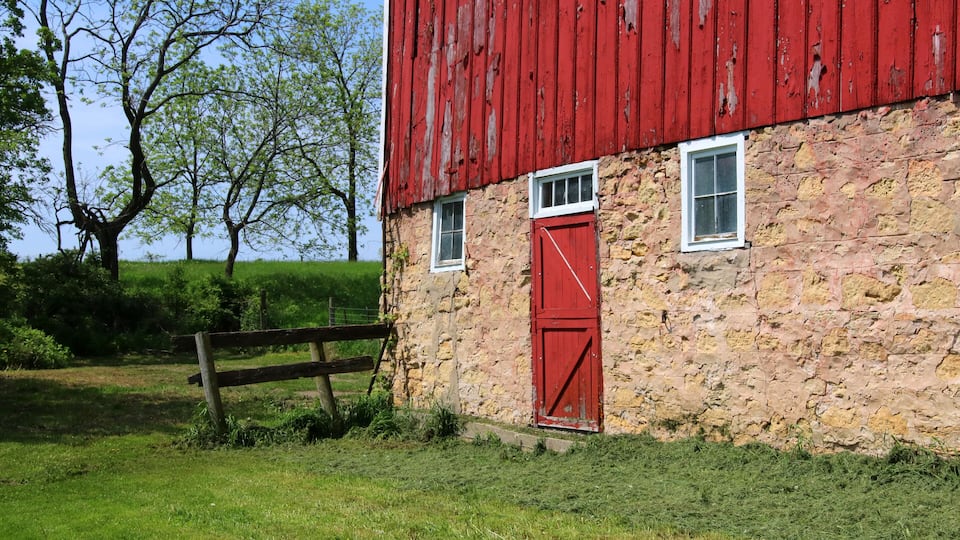 A red barn with a stone wall, a wooden fence, and green trees in the background.