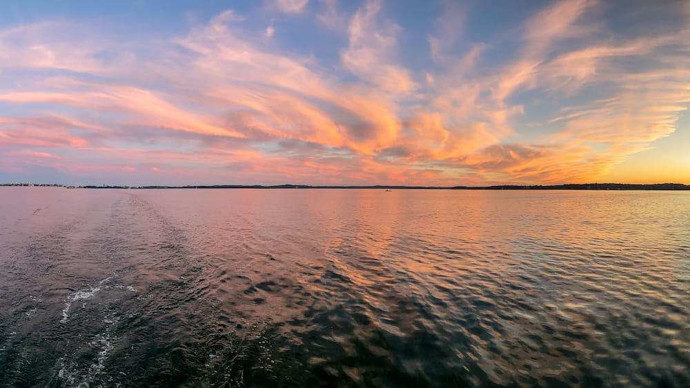 Une étendue d’eau calme reflétant un ciel au coucher du soleil, parsemé de nuages.