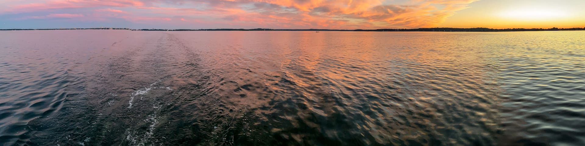 A calm body of water reflecting a sunset sky with scattered clouds.