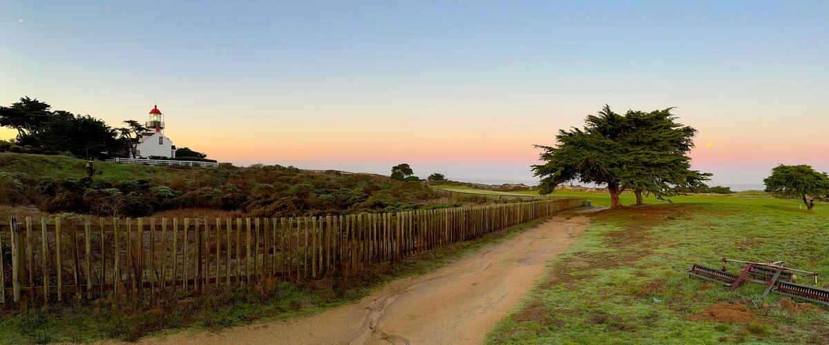A coastal path with a lighthouse, wooden fence, and trees.