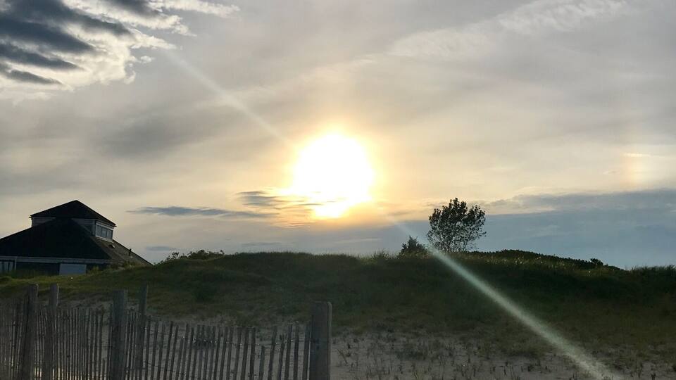A beach with a wooden fence, a house, and a sunset.
