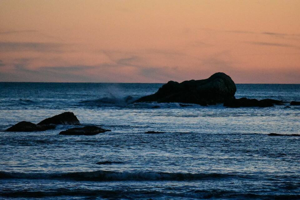 A rocky coastline at sunset with waves crashing against the rocks.