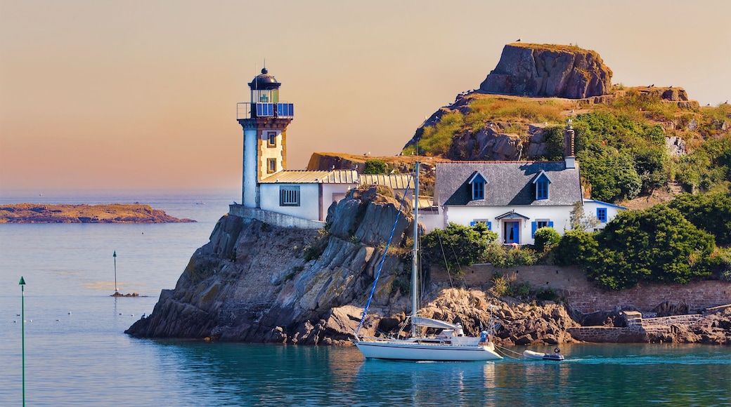 A coastal village with a lighthouse, a sailboat, and a prominent rock formation.