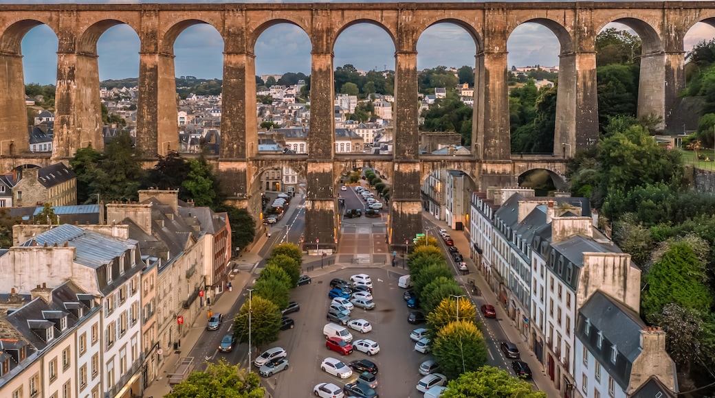 A historic stone bridge with multiple arches spanning a river, surrounded by urban buildings and greenery.