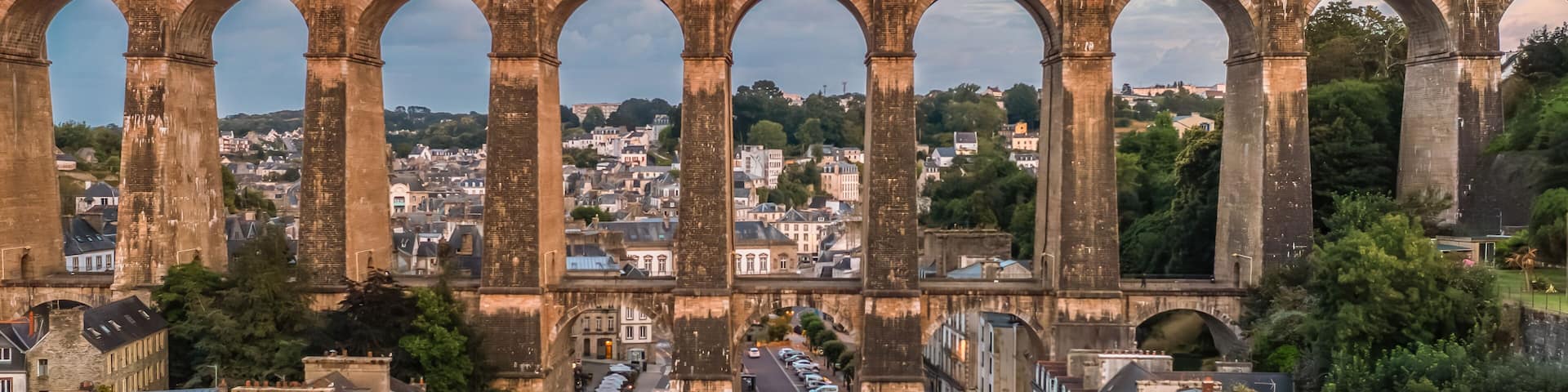 A historic stone bridge with multiple arches spanning a river, surrounded by urban buildings and greenery.