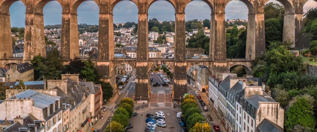 A historic stone bridge with multiple arches spanning a river, surrounded by urban buildings and greenery.