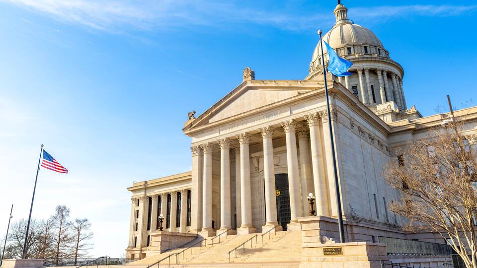 A neoclassical building with a dome and columns, an American flag, and a sign reading 'Oklahoma State Capitol.'