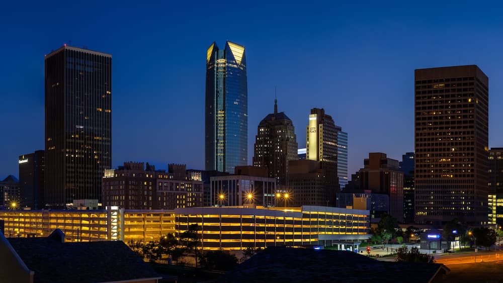 A city skyline at dusk with illuminated buildings and a prominent modern skyscraper.