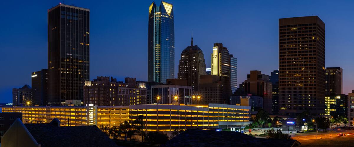 Un horizonte urbano al anochecer con edificios iluminados y un moderno rascacielos destacado.