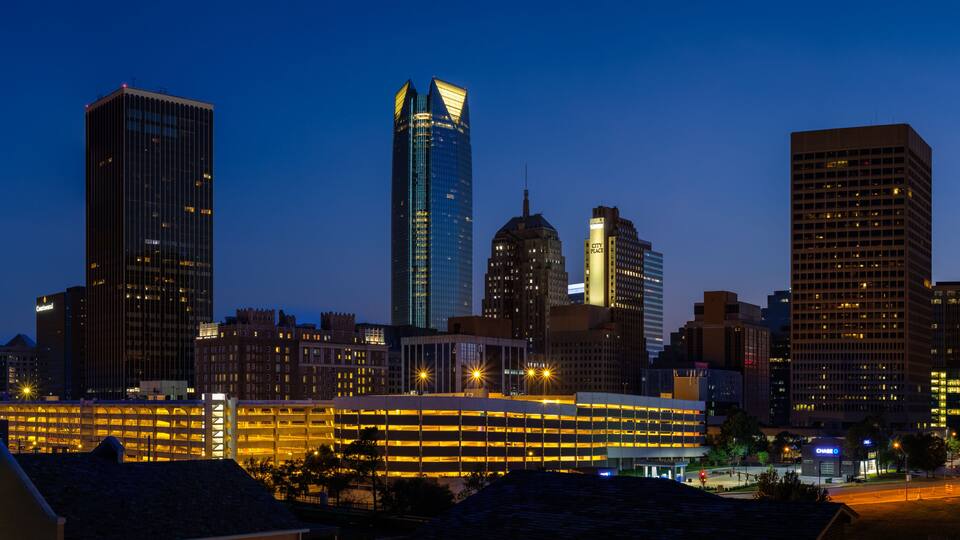 A city skyline at dusk with illuminated buildings and a prominent modern skyscraper.