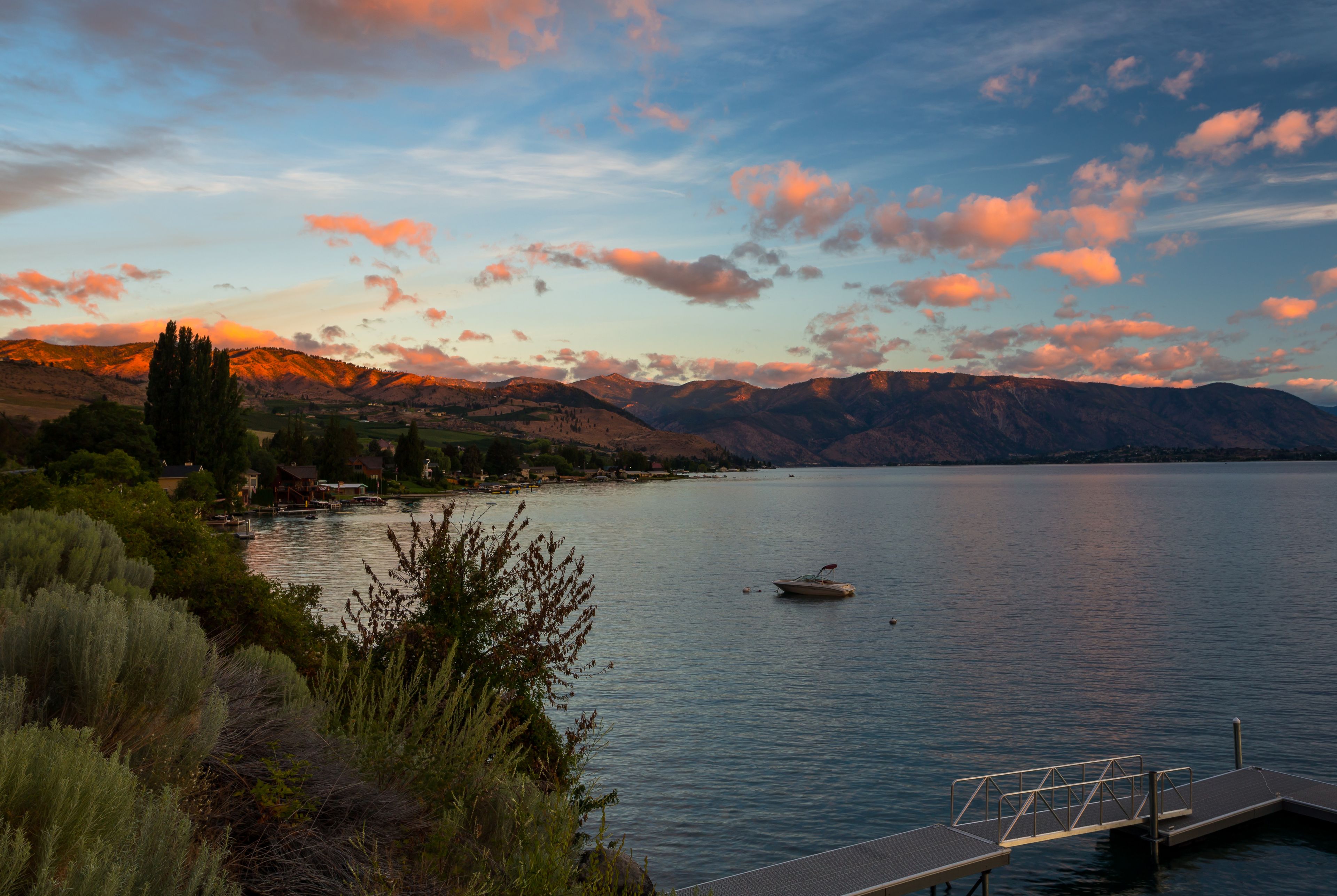 A calm lake with a boat, surrounded by mountains and a dock.