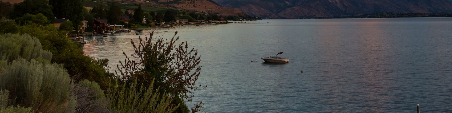 A calm lake with a boat, surrounded by mountains and a dock.