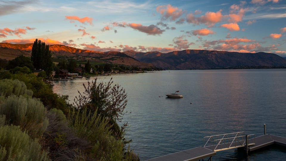 A calm lake with a boat, surrounded by mountains and a dock.