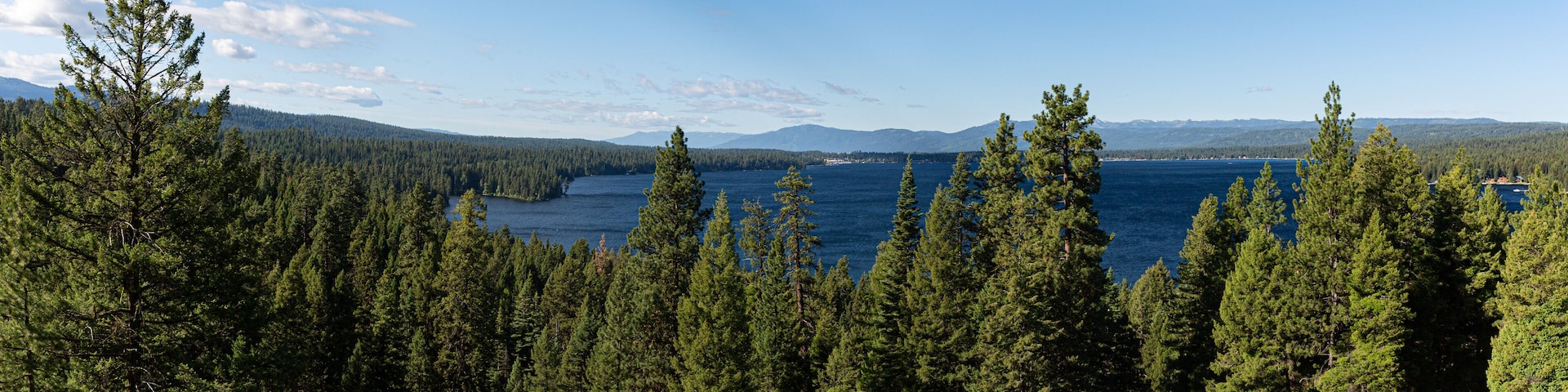 A lake surrounded by dense forests and distant mountains under a clear sky.