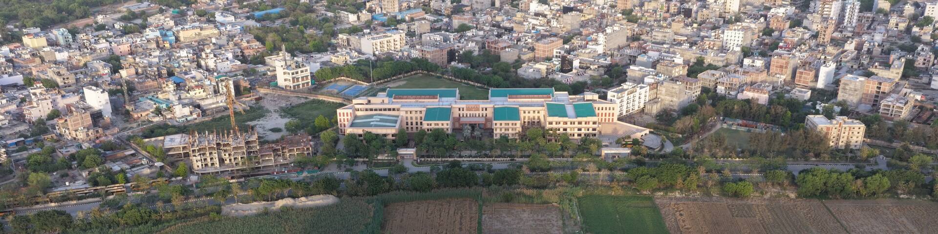 Aerial view of a lush green golf course, agricultural fields, and a large modern building complex with the urban skyline in the background Gurugram, Haryana, India.