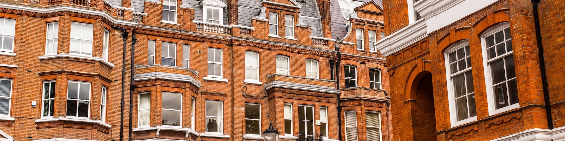 Una hilera de casas adosadas victorianas de ladrillo rojo, con ventanas salientes y detalles blancos.