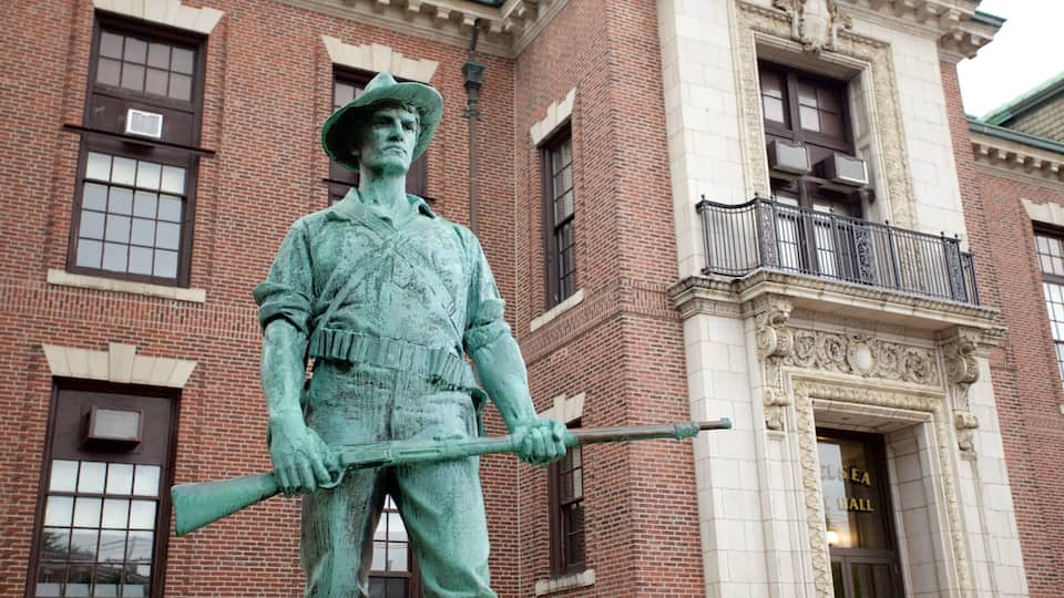 A statue of a man in uniform holding a rifle in front of a brick building with a balcony.