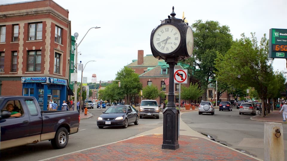 A busy street with a large clock, brick buildings, and cars.