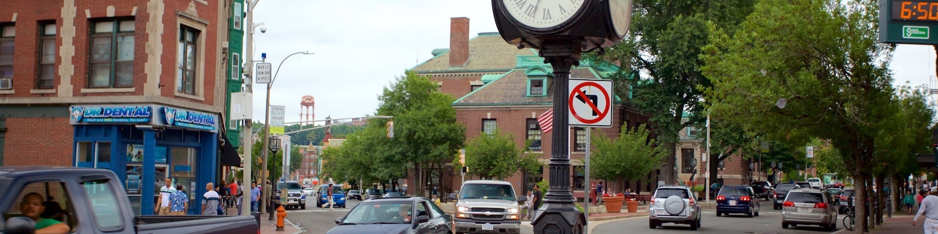 A busy street with a large clock, brick buildings, and cars.