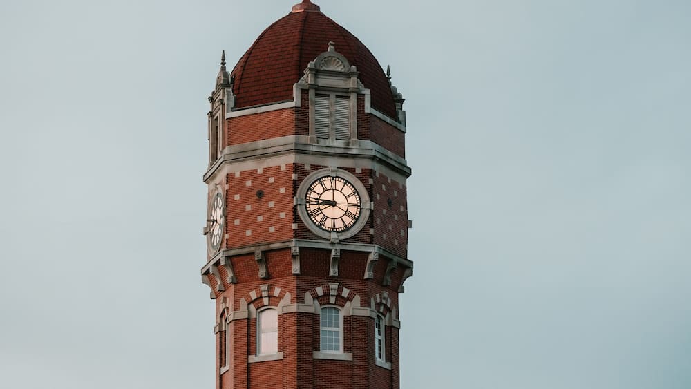 Close-up of a red brick clock tower with a domed roof at dusk