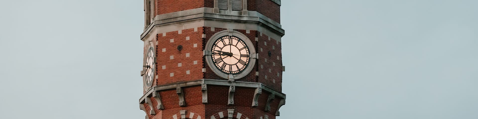 Close-up of a red brick clock tower with a domed roof at dusk