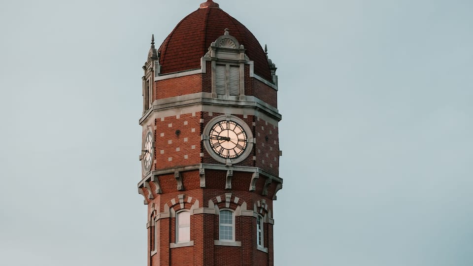 A tall brick clock tower with a dome roof and a large clock face.