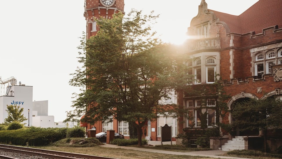 A brick building with a clock tower, railroad tracks, and trees.