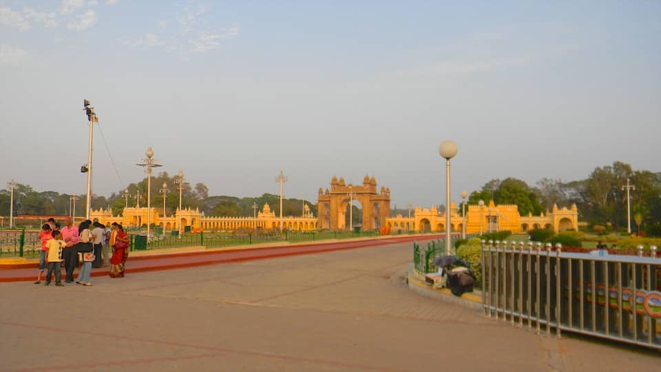 A large, ornate gate with intricate architecture, a paved walkway, and a green fence.