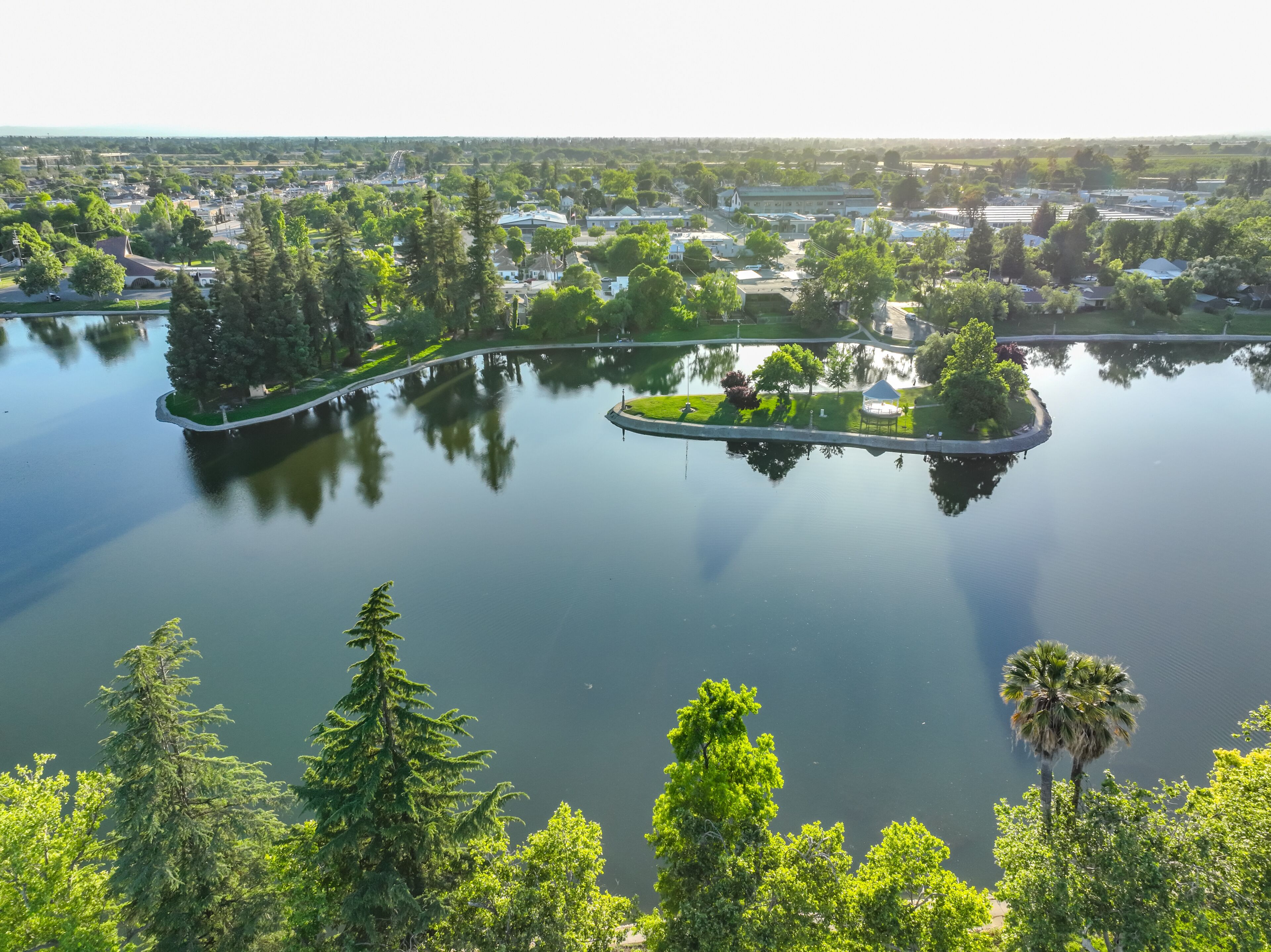 A lake with islands, surrounded by dense greenery and residential buildings.