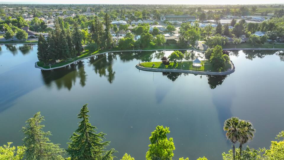 A lake with islands, surrounded by dense greenery and residential buildings.