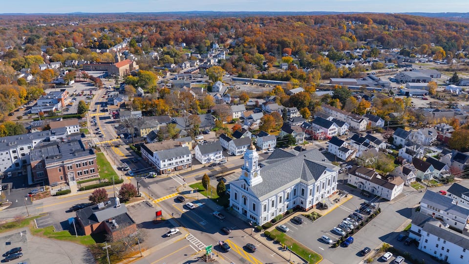 An aerial view of a town with a prominent white church with a clock tower, surrounded by residential houses and autumn-colored trees.