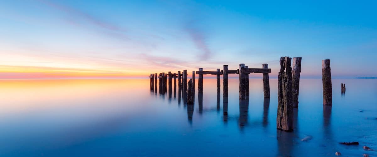 A sunset over a calm body of water with wooden posts in the foreground.