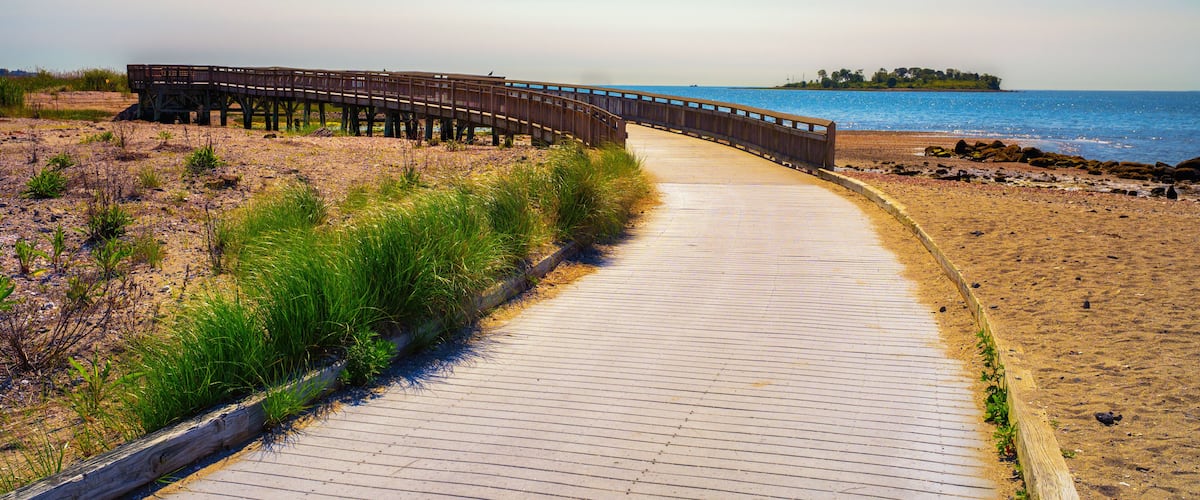 A wooden boardwalk leading to a beach with a wooden pier extending into the water.