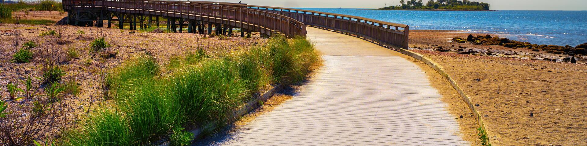 A wooden boardwalk leading to a beach with a wooden pier extending into the water.