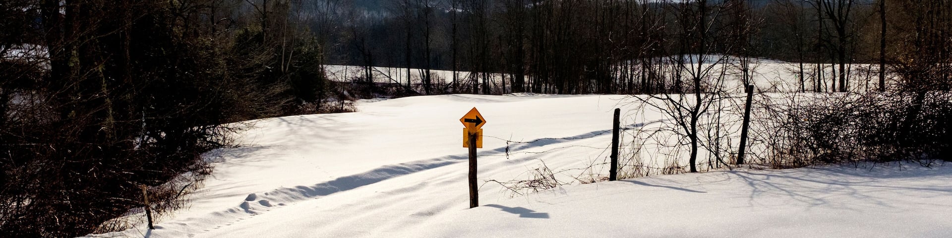 Arrow symbol on snow covered landscape against cloudy sky