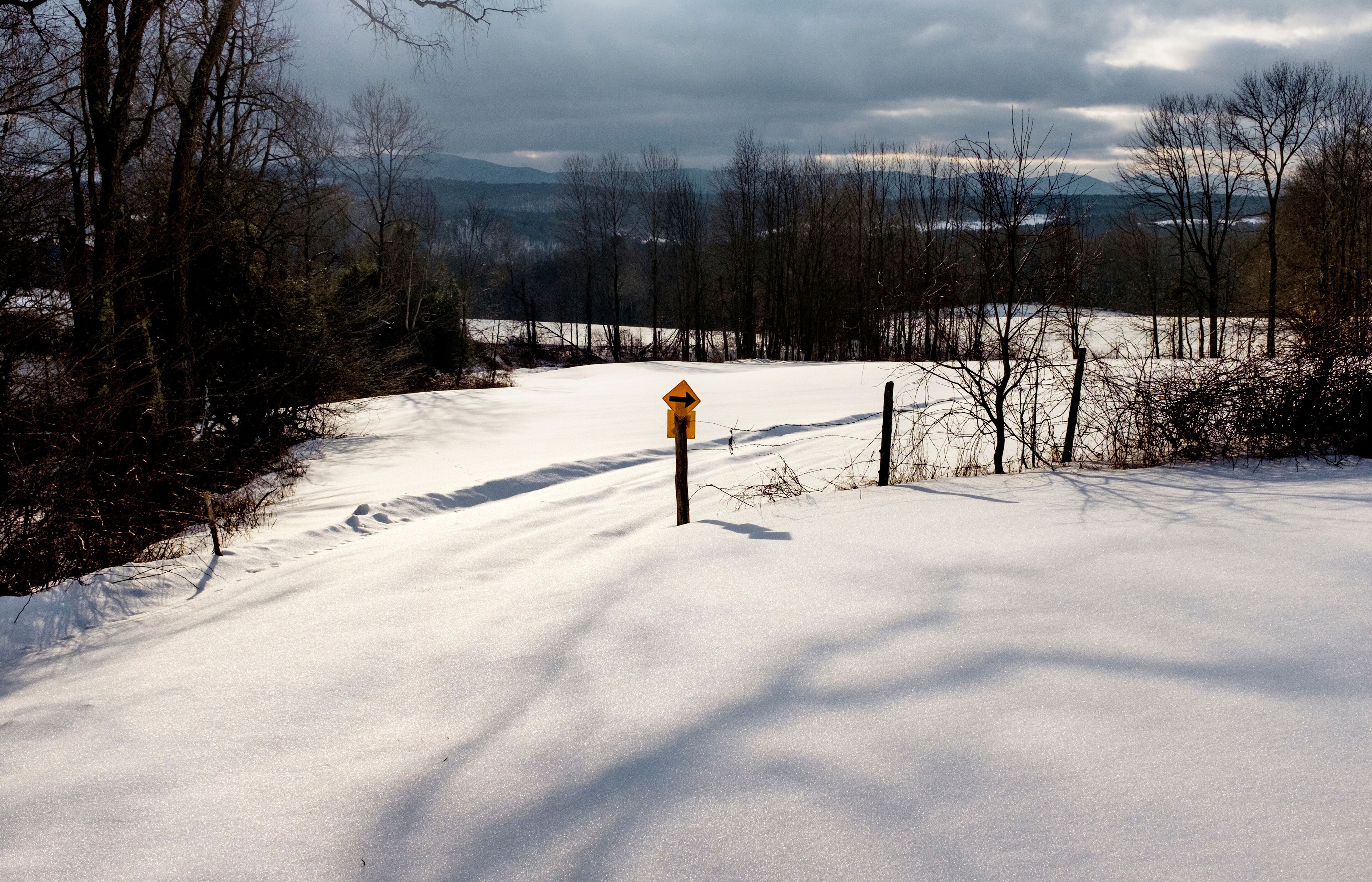 A snow-covered landscape with a wooden post and a yellow sign in the center.