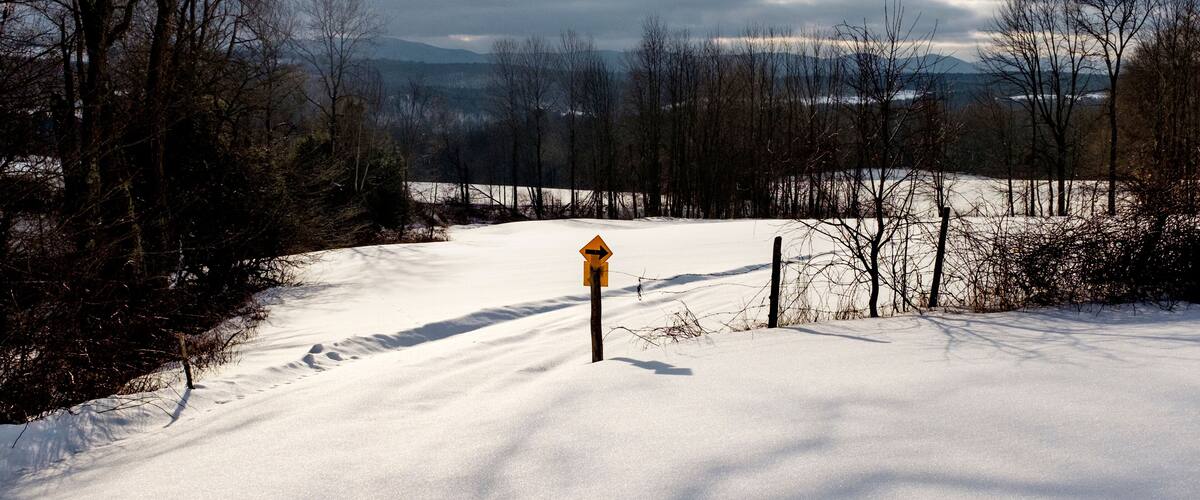 A snow-covered landscape with a wooden post and a yellow sign in the center.