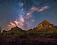A starry night sky over a rocky mountain range with sparse vegetation.