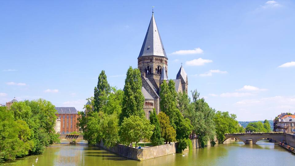 A historic tower with a pointed roof, surrounded by lush green trees and a calm river.