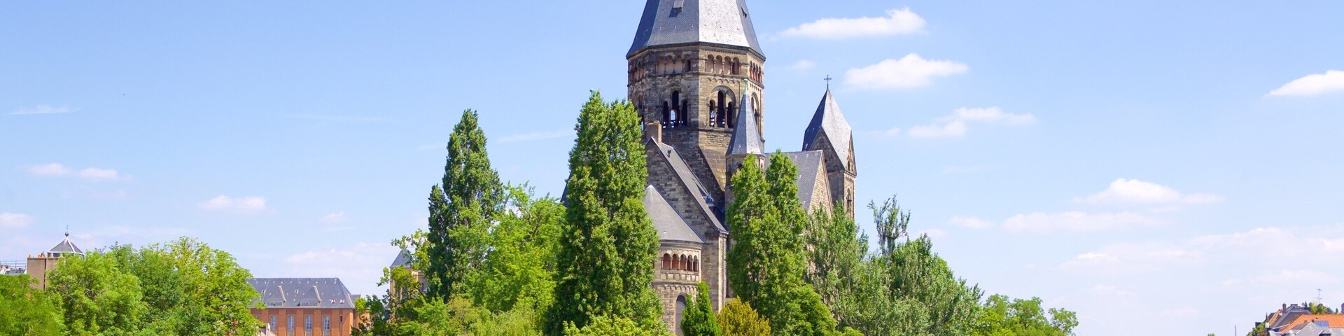 Uma torre histórica com telhado pontiagudo, rodeada por árvores verdes exuberantes e um rio calmo.