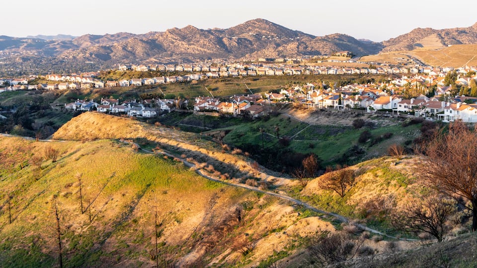 A hillside town with houses, a winding road, and mountains in the background.