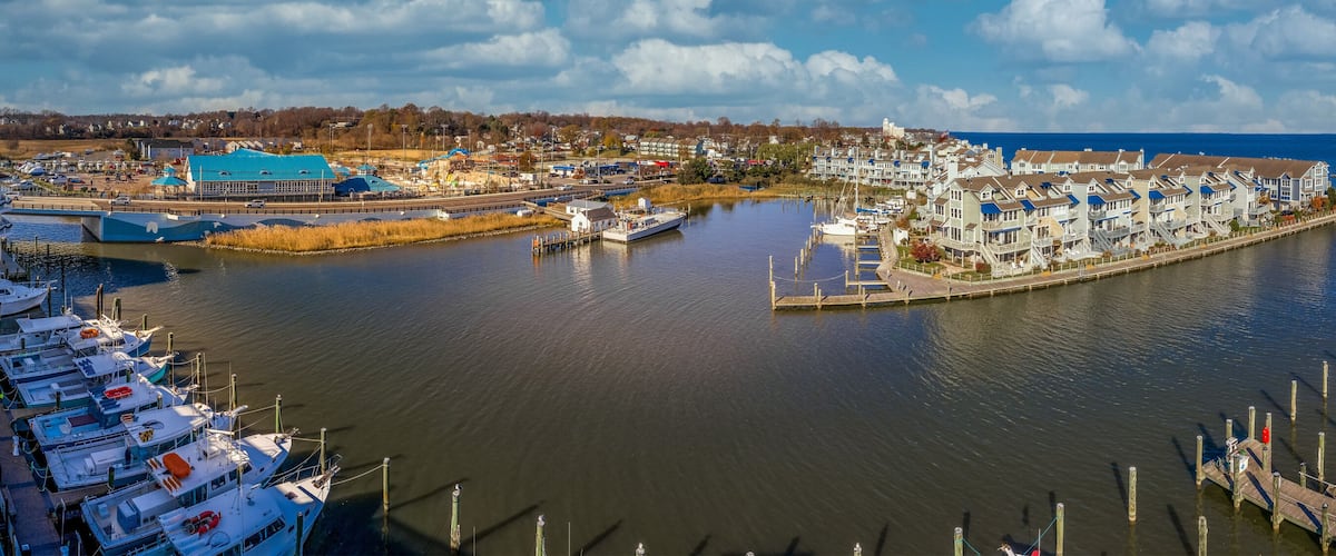 A harbor with boats docked, a pier, and a row of houses along the water.