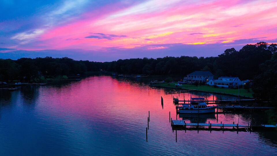 A sunset over a calm lake with a dock and houses on the shore.