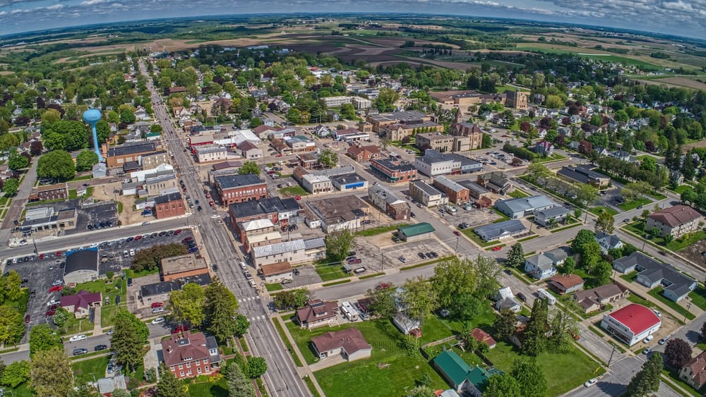 An aerial view of a small town with a central street, surrounding buildings, and green fields.