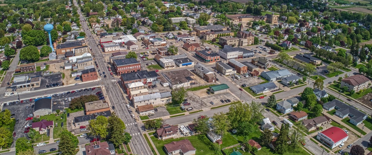 An aerial view of a small town with a central street, surrounding buildings, and green fields.