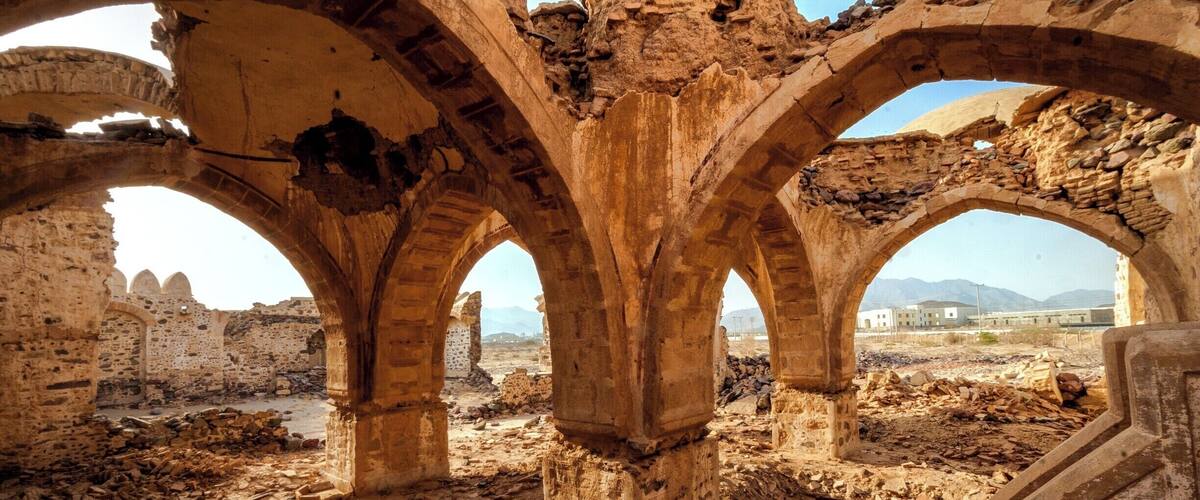 An ancient stone archway with visible damage and surrounding ruins.