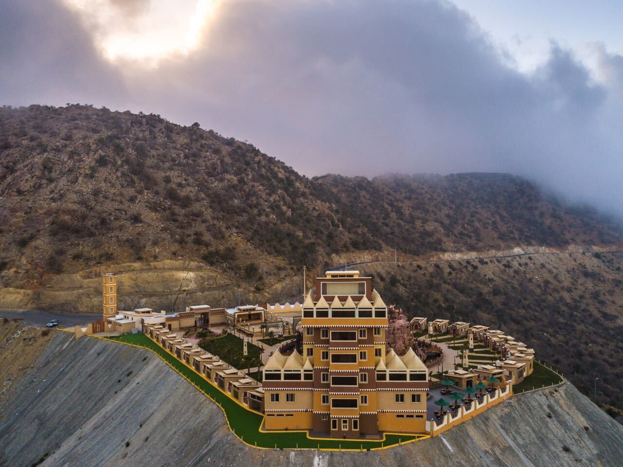 A large, multi-tiered building complex with a central tower, surrounded by a mountainous landscape.